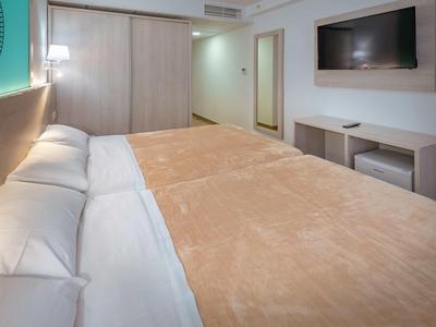 Habitación de hotel moderna con cama grande, televisor de pared y muebles sencillos de madera.