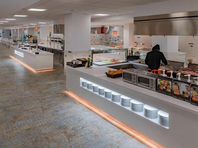 Cocina moderna de hotel con mostradores blancos, estación de cocina y amplia iluminación.