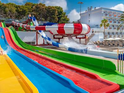 Bunte Wasserrutschen in einem Wasserpark bei einem Hotel mit Liegestühlen im Hintergrund.
