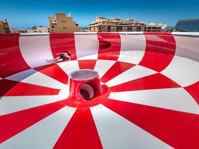 Piscina de tobogán de agua a rayas rojas y blancas bajo un cielo claro en un hotel.