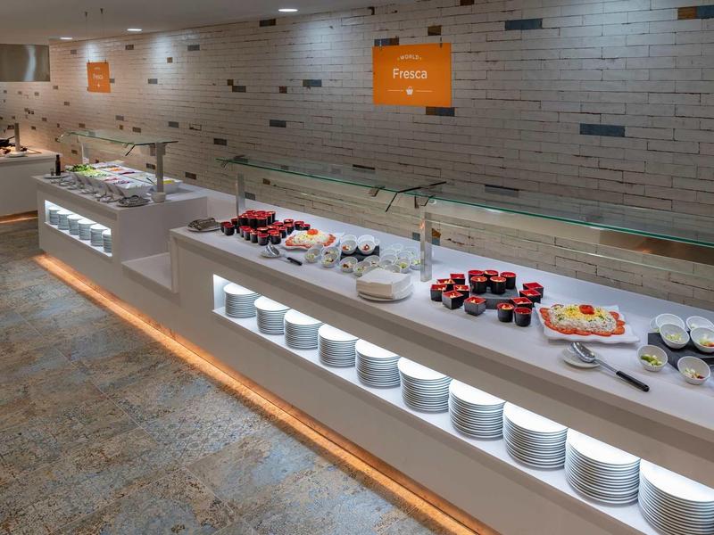 Buffet con diversos alimentos sobre mesa larga con iluminación en un espacio moderno.