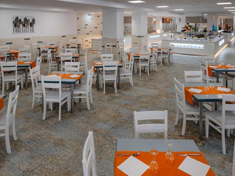 Amplio comedor con mesas blancas, manteles naranjas y sillas de madera en hotel moderno