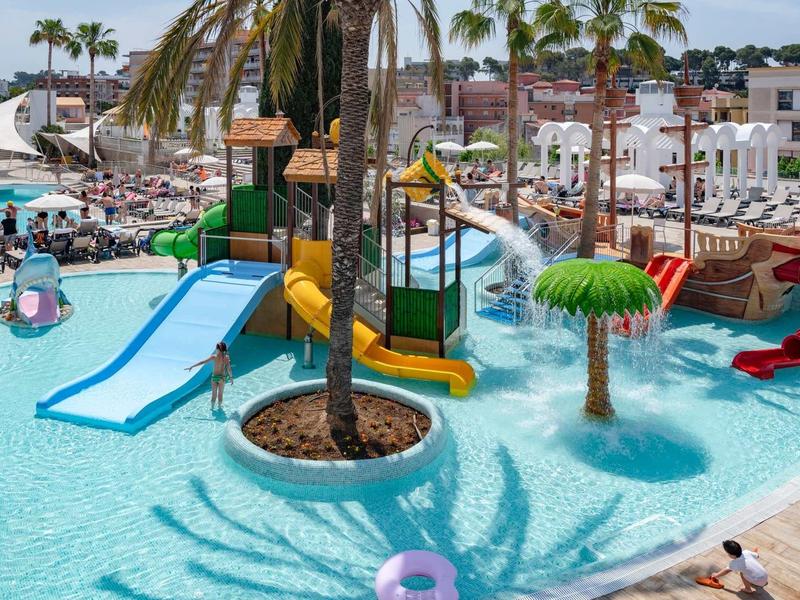 Colorido parque acuático con toboganes y palmeras en una piscina de hotel bajo un cielo soleado.
