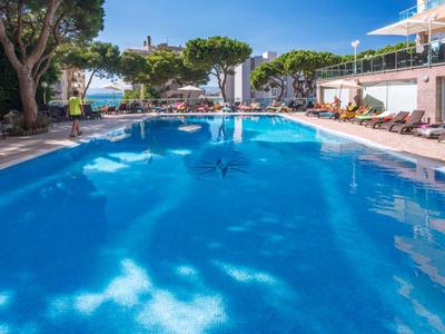 Large blue hotel pool with sun loungers and umbrellas on a sunny day.