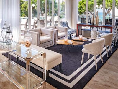 Bright living room with comfortable armchairs, glass and wooden furniture, large carpet, and panoramic windows.