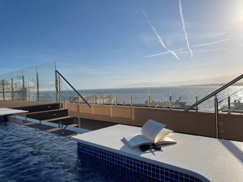 Bazén s otevřenou terasou a výhledem na moře pod jasnou oblohou s kondenzačními stopami.