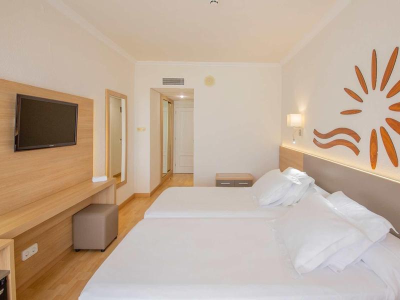 Světý hotelový pokoj s velkou manželskou postelí, dřevěnou podlahou a moderním nástěnným dekorem.