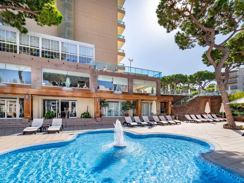 Hotel s venkovním bazénem, slunečníky a lehátky na slunném místě.