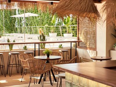 Accogliente bar dell'hotel con sgabelli, sedie in rattan e vista sul giardino verde.