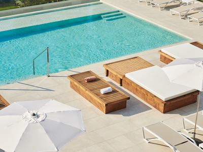 Area piscina moderna con lettini, ombrelloni e acqua limpida e blu.