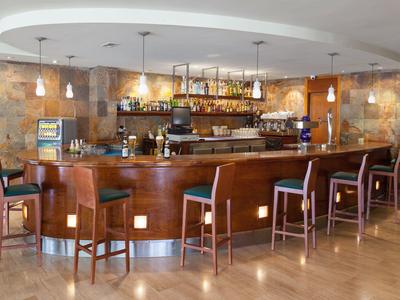 Area bar moderna con bancone in legno, sgabelli e illuminazione calda.