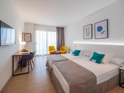 Camera d'hotel moderna con due letti, scrivania, area salotto e balcone luminoso.
