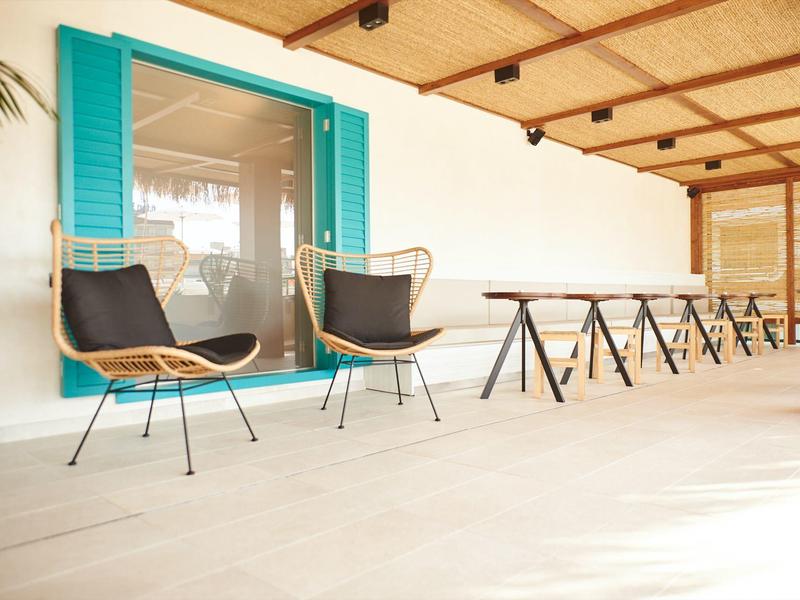 Una terrazza con due sedie bianche con cuscini neri davanti a una finestra con persiane blu.