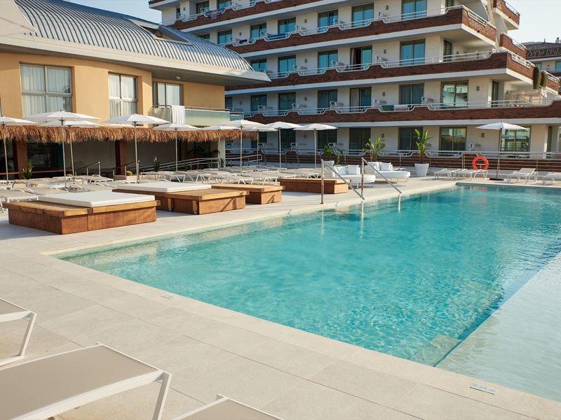 Piscina d'hotel moderna con lettini e ombrelloni davanti a un edificio a più piani