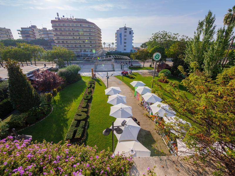 Vista su un giardino con ombrelloni bianchi e edifici sullo sfondo sotto un cielo limpido.