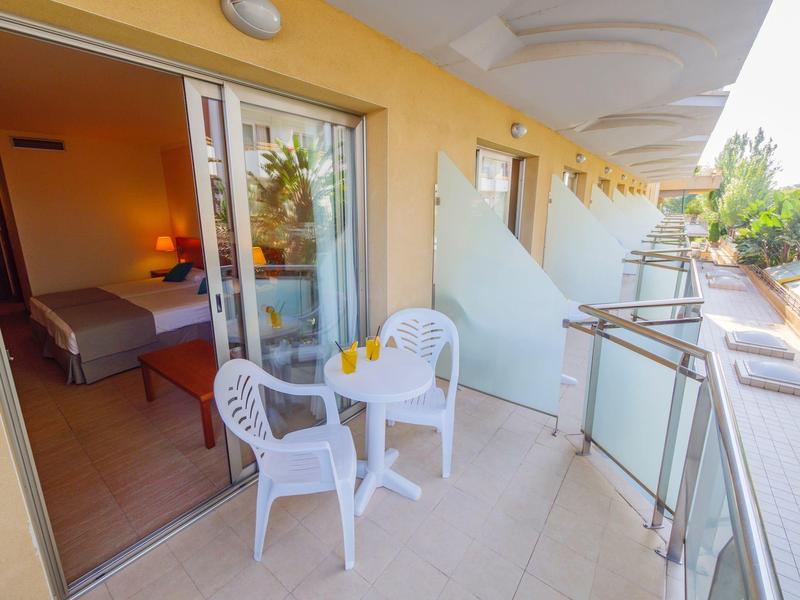 Balcone con tavolo, sedie e vista su una camera da letto con porta scorrevole aperta.