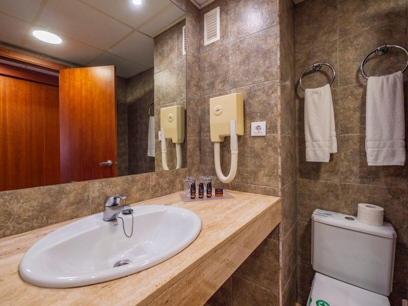 Bagno d'hotel moderno con grande specchio, lavabo, asciugacapelli e articoli da toilette.