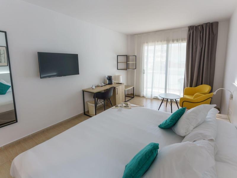 Camera d'albergo moderna con letto matrimoniale, scrivania, TV a parete e poltrona vicino alla finestra.