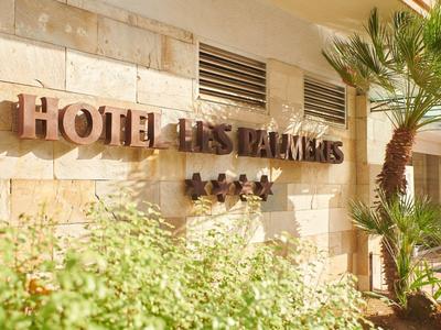 Fassade des Hotels Les Palmiers mit einem Schild und Palmen im Vordergrund