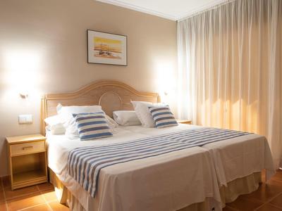 Světý hotelový pokoj s velkou manželskou postelí, dvěma nočními stolky a bílými závěsy.