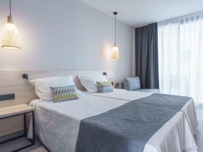 Moderní hotelový pokoj se dvěma jednolůžky, závěsnými lampami a velkým světlým oknem.