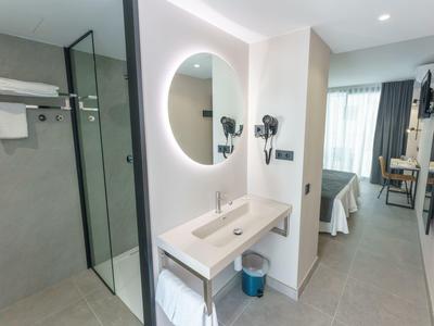 Světý hotelový pokoj s moderní koupelnou, osvětleným zrcadlem a průhlednou sprchou.