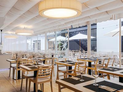 Moderní světlá restaurace s dřevěnými židlemi a prostřenými stoly pod velkým svítidlem.