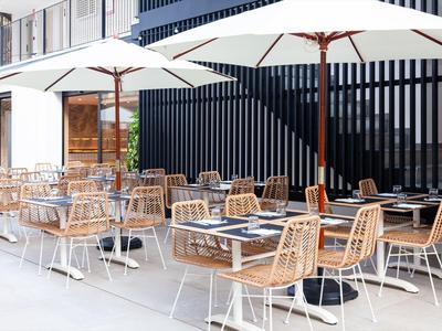 Moderní venkovní prostor kavárny se dřevěnými židlemi, stoly a velkými slunečníky.