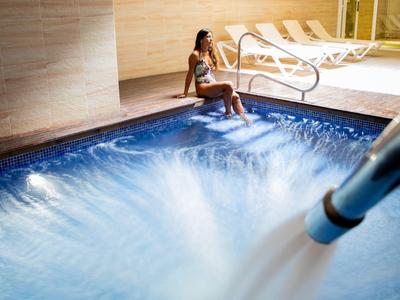 Žena sedí na okraji osvětleného vířivého bazénu s proudem vody.