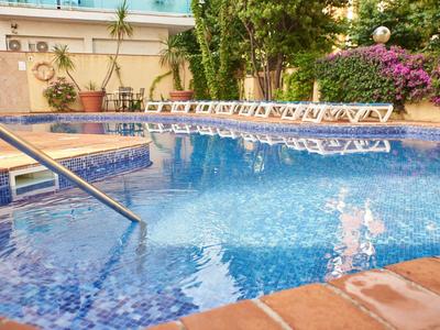 Čistý bazén s modrou vodou a bílými lehátky vedle kvetoucích rostlin.