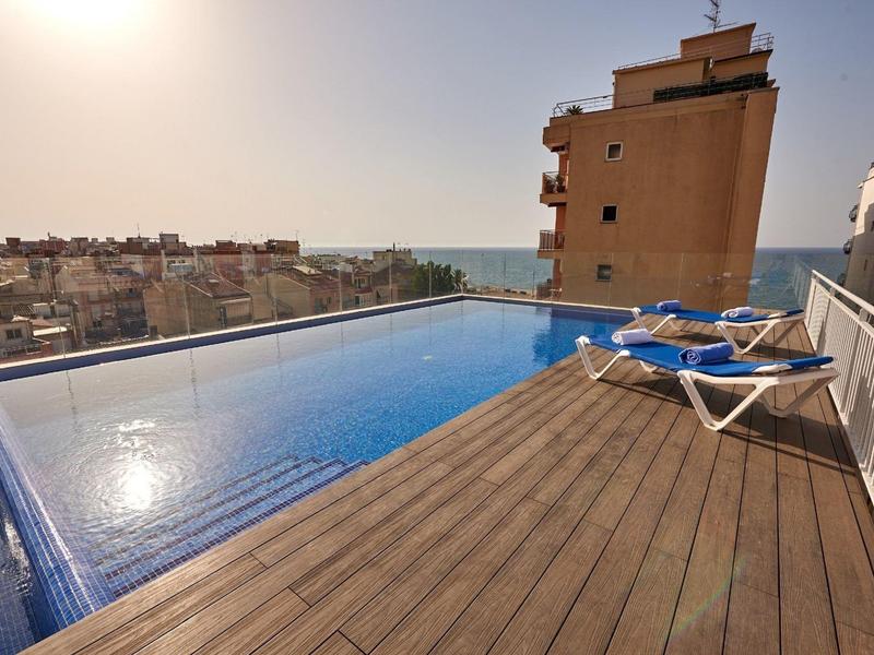 Nekonečný bazén na střešní terase s výhledem na moře a lehátky při západu slunce.