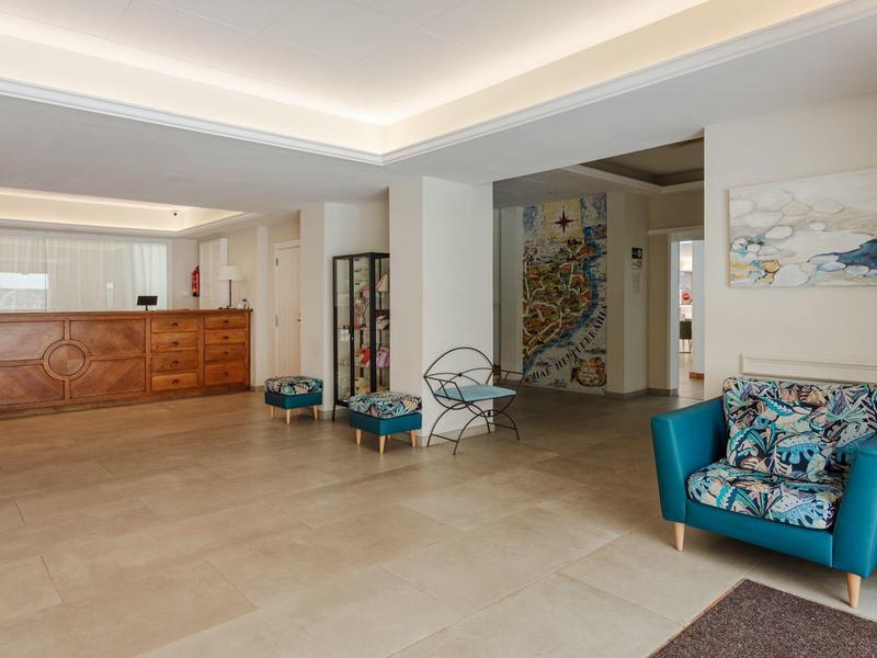 Moderní hotelová recepce s posezením a dekorativní nástěnnou malbou v světlé místnosti.