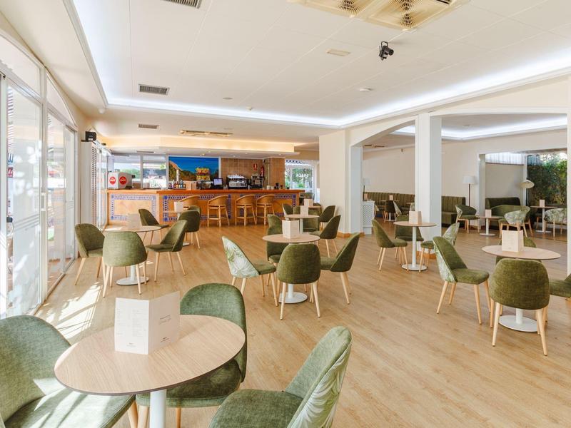 Světý a moderní interiér hotelového baru s stolem, zelenými křesly a dřevěným barem