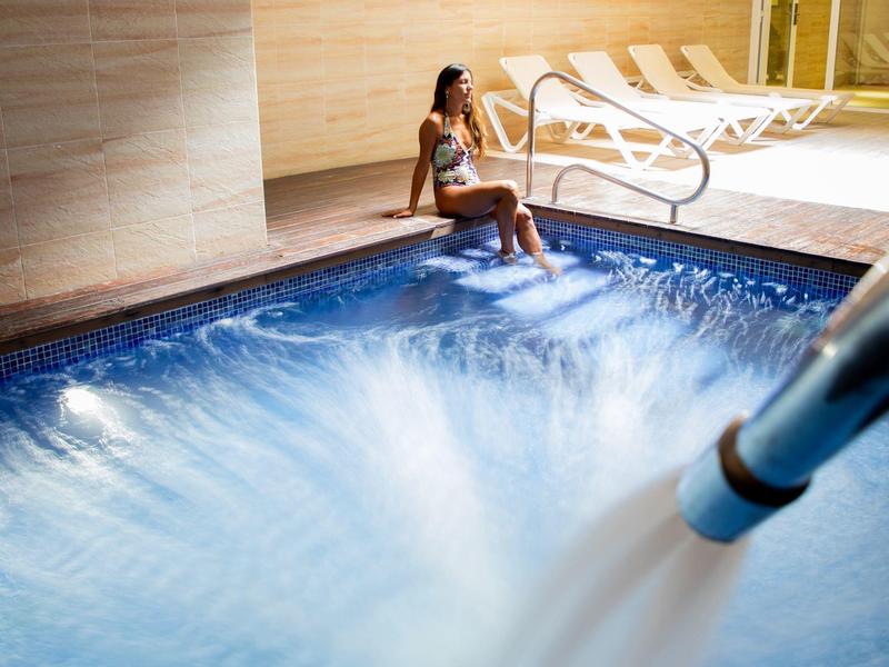 Žena sedí na okraji osvětleného vířivého bazénu s proudem vody.