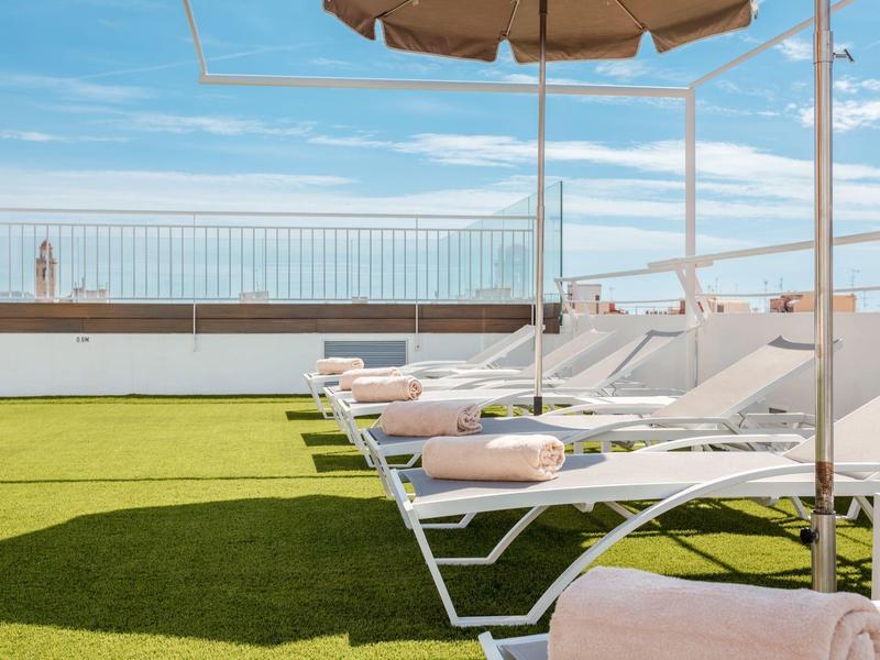 Bílé lehátka s růžovými ručníky na zeleném trávníku pod slunečníky za modré oblohy.