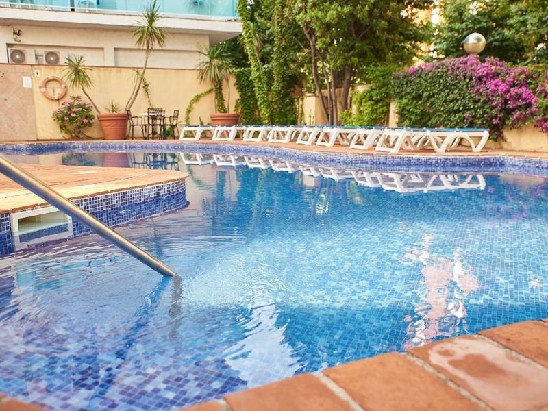 Čistý bazén s modrou vodou a bílými lehátky vedle kvetoucích rostlin.