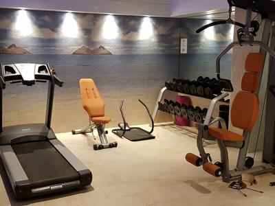 Moderner Fitnessraum mit Laufband, Trainingsbank, Hanteln und Kraftmaschine in gedämpftem Licht.