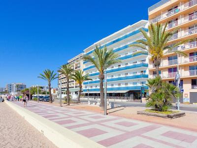 Promenade mit Palmen, Sandstrand, modernen mehrstöckigen Gebäuden und blauem Himmel.
