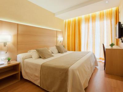 Gemütliches Hotelzimmer mit Doppelbett, Schreibtisch und großen Fenstern mit Vorhängen.