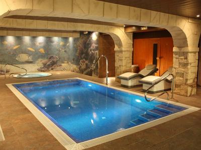 Innen-Schwimmbad mit rechteckigem Becken, Steinsäulen, Wandgemälde und zwei Liegestühlen.