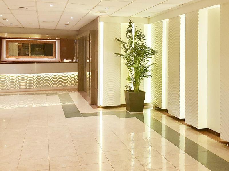 Helle Empfangshalle mit glänzendem Boden, Pflanzen und beleuchtetem Tresen.