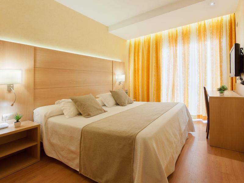 Gemütliches Hotelzimmer mit Doppelbett, Schreibtisch und großen Fenstern mit Vorhängen.