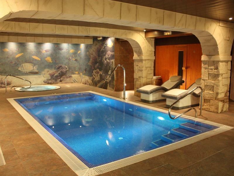 Innen-Schwimmbad mit rechteckigem Becken, Steinsäulen, Wandgemälde und zwei Liegestühlen.