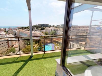 Balcony with green carpet, glass railing, and view of city and pool under clear sky.