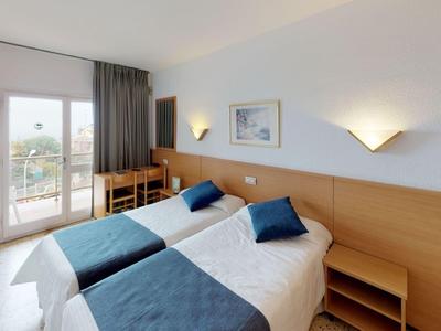 Hotel room with two single beds, blue pillows, desk, and balcony with outdoor view.