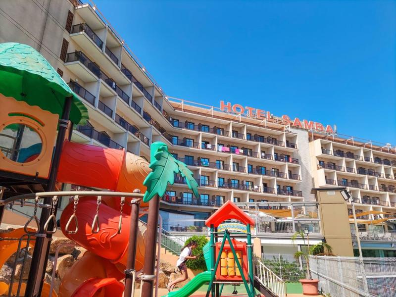 Multi-story hotel with playground and red slide under clear sky.