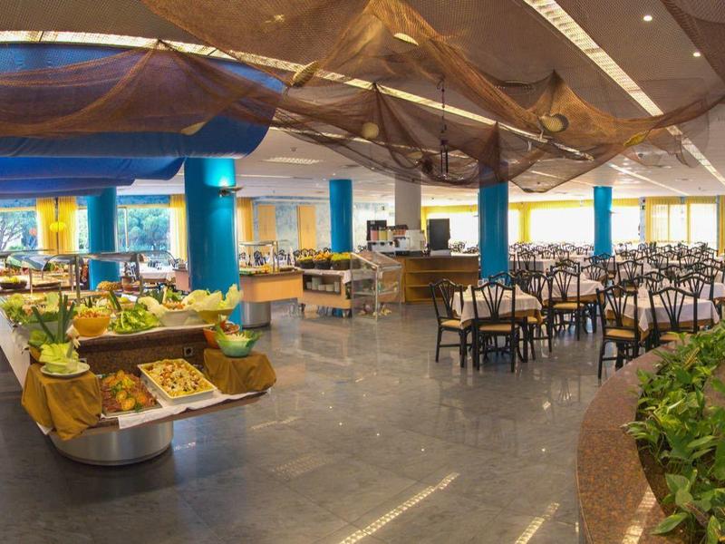 Duża jasna jadalnia z wieloma stolikami i wystawą owoców i warzyw.