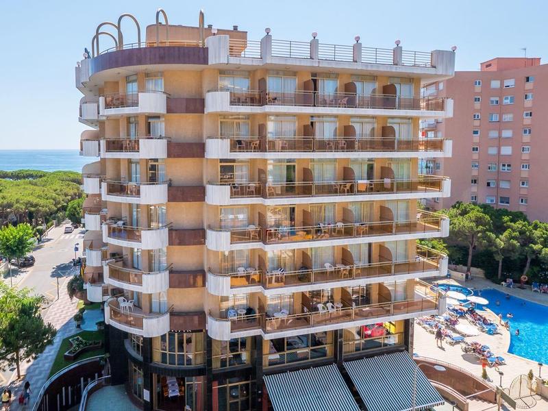 Nowoczesny wielopiętrowy hotel z balkonami, otoczony basenami i zielenią nad morzem.