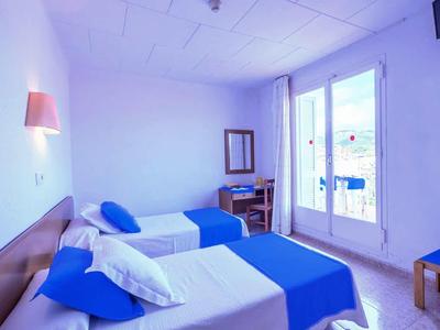 Camera d'hotel luminosa con due letti singoli, accenti blu e balcone con vista mare.