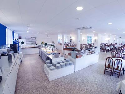 Duża jasna sala śniadaniowa z bufetem oraz wieloma stołami i krzesłami.